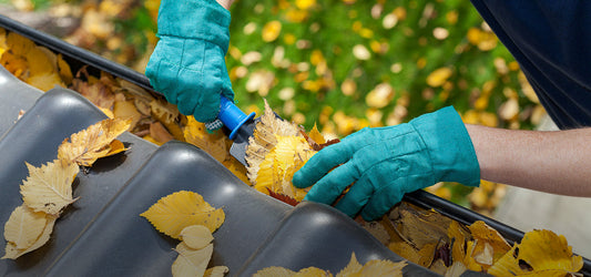 2 gloved hands cleaning the gutter with a garden tool