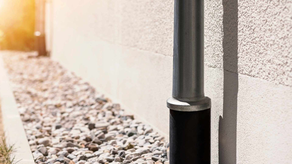 Commercial rain gutter downspout carries debris into a buried storm drainage pipe and can clog.