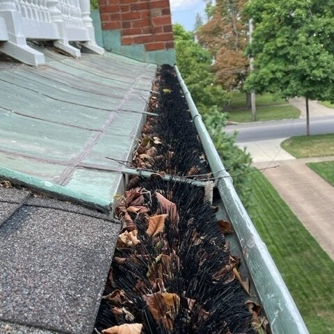 Traditional green petina copper gutter with brush gutter guard clog protection.
